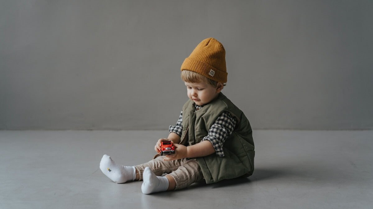 Criança sentada no chão, com roupa charmosa, colete, calça e toca
